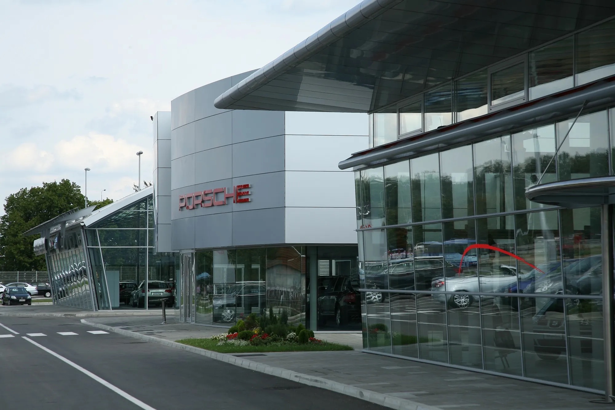 Auto salon Porsche Ada — zaobljena staklena fasada salona i paviljon sa natpisom Porsche