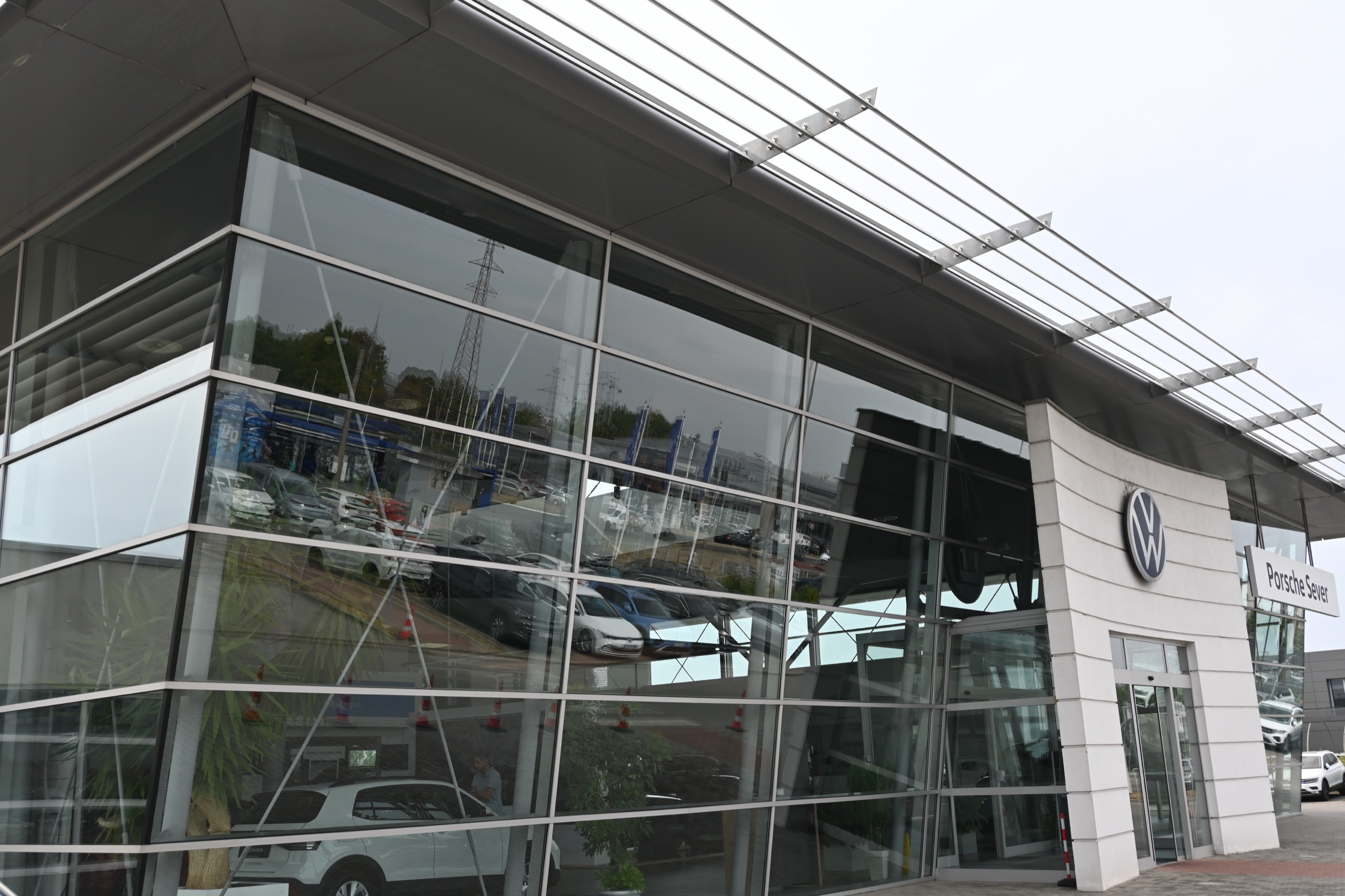 Auto salon Volkswagen — ugao staklene fasade u kojoj se ogleda parking, nadstrešnica od lamela iznad